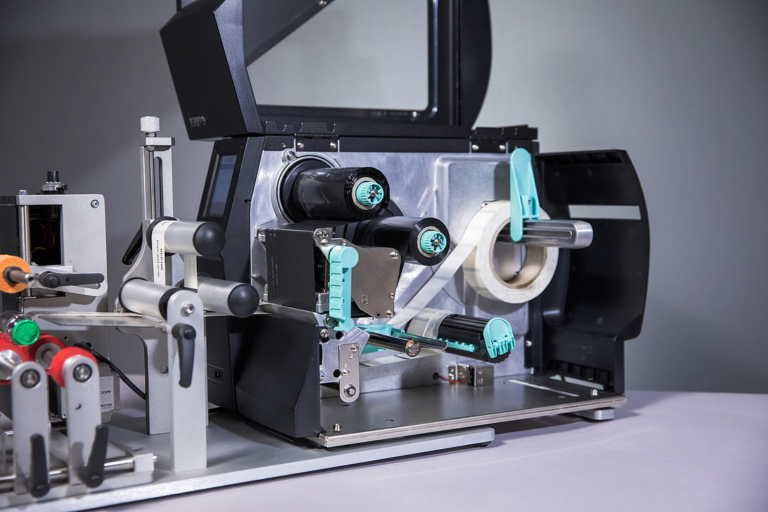 An open thermal transfer label printer showing the label roll and ribbon path.