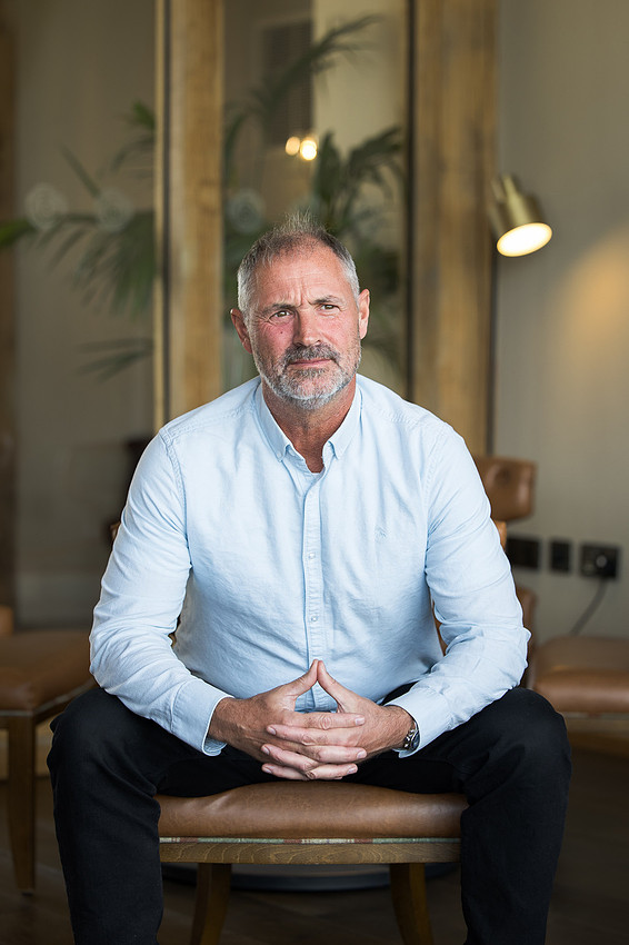Portrait of a bearded man in a light blue shirt, seated indoors.