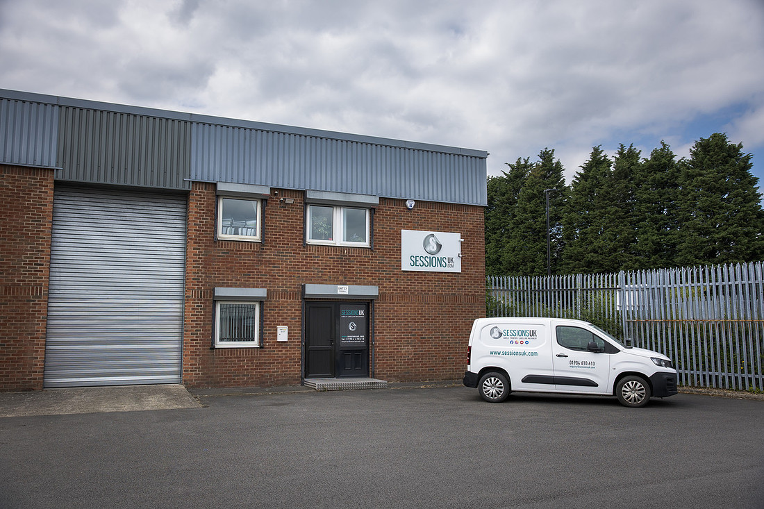The brick industrial unit seen from across the yard, with the Sessions UK van parked by the fence.