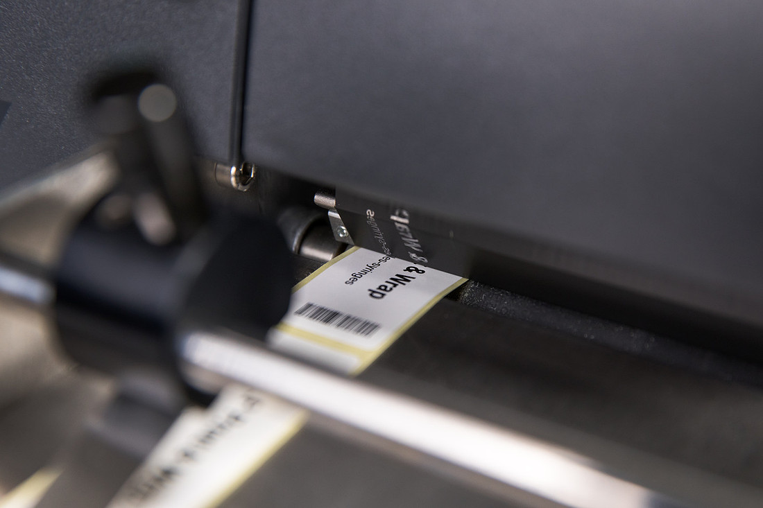 Close-up of a printed label passing over the black roller inside a benchtop labeller.