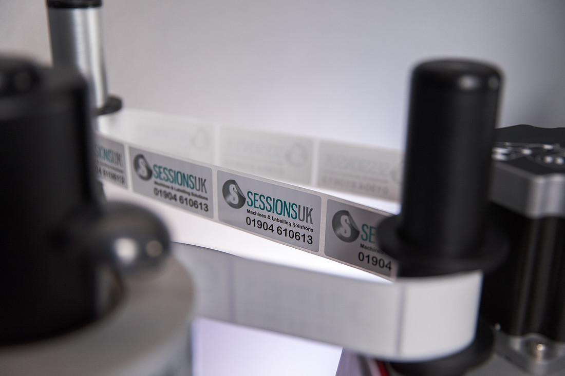 Close-up of a web of Sessions UK labels feeding through the applicator of a labelling machine.