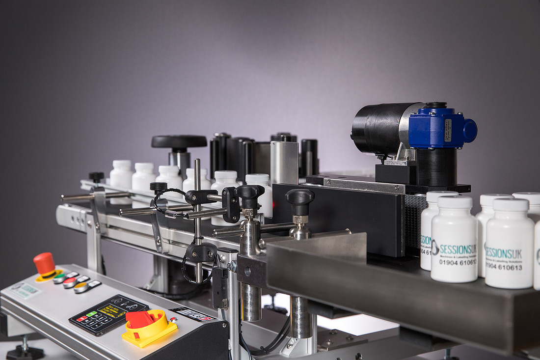 An inline bottle labelling machine on a bench, running white bottles past the labelling head.